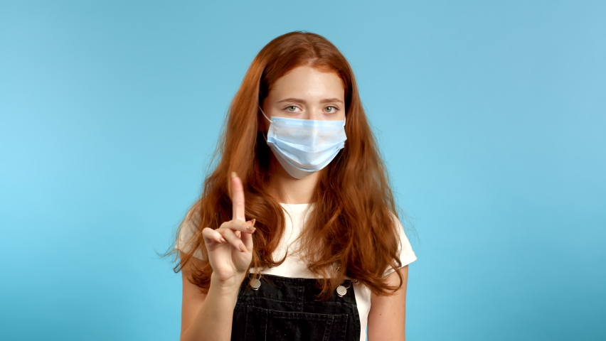 Pretty Woman in medical protective mask disapproving with no finger sign make negation gesture. Denying, Rejecting, Disagree, Portrait of woman on blue background. | Shutterstock HD Video #1059889811