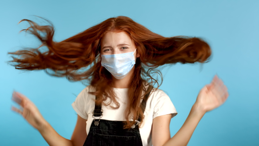 Beautiful woman in medical protective mask dancing energetically and actively on blue studio background.  Party, happiness, freedom, youth concept. | Shutterstock HD Video #1059889832