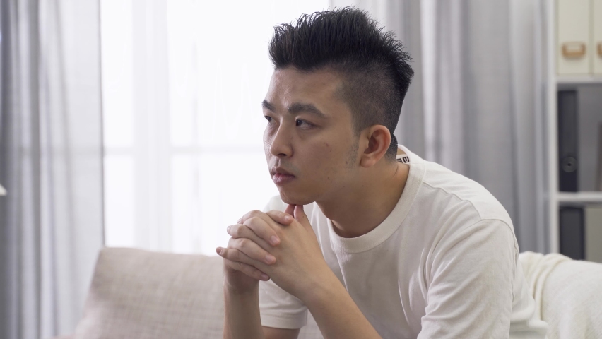 Close up asian young man gazing into distance in contemplation. with hands crossed and clasped thinking about future | Shutterstock HD Video #1059894515