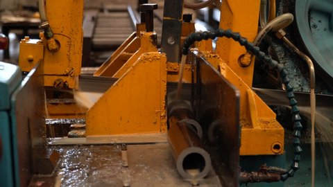 Industrial band saw, cutting metal pipe, coolant in yellow scene, industrial tools
