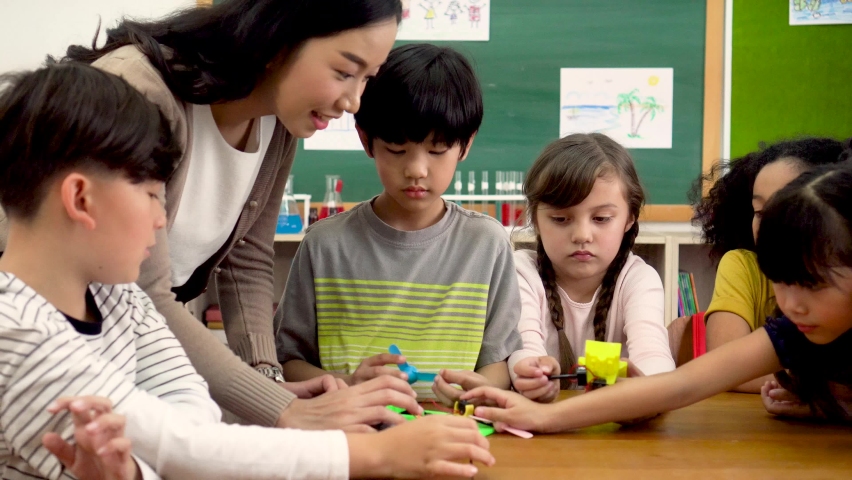 Young woman working in school helping multiethnic children make toy cars, learning about mechanics, stem. Asian school teacher assisting elementary students in science classroom Royalty-Free Stock Footage #1059895964