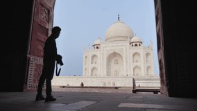 A young man or male photographer standing and taking a picture of a beautiful Taj Mahal Mausoleum with professional DSLR camera. A solo traveller or tourist clicking photos on his travel adventure 
