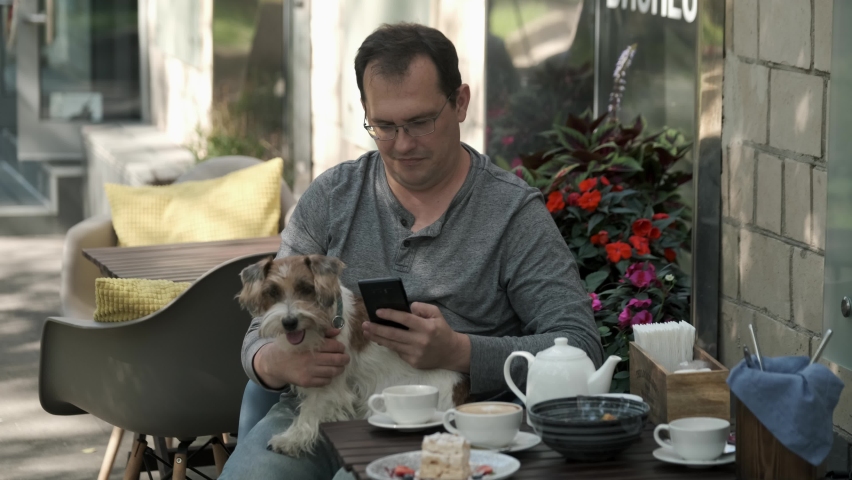 Man using mobile phone with small jack russell dog lying in his lap