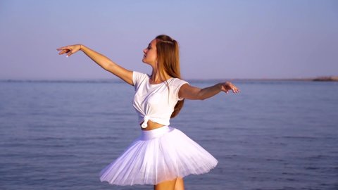 Woman in white dances classic ballet in calm water by beach