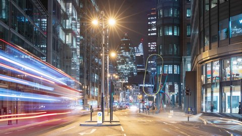 Night time lapse of a busy road in London, UK with cars and buses zooming past and famous skyscrapers in the background