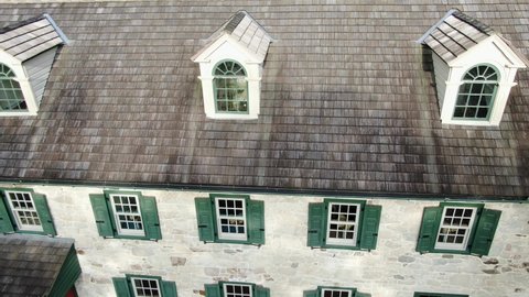 Typical traditional old stone farmhouse home. Germanic architecture in Pennsylvania USA. Green shutters, burgundy door. Dormers and cedar shingle roof. Aerial drone view.