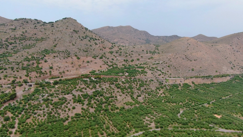 Arid mountains and green tree fields of Crete Island. Aerial forward