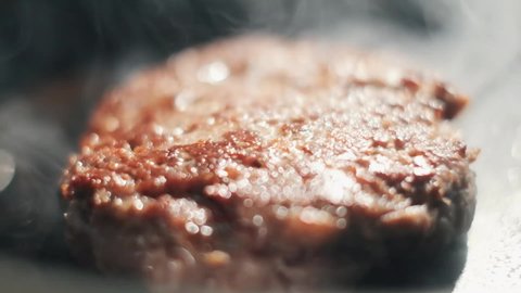 Chef preparing the burger, frying the meat on the pan. Frying hamburger or cheeseburger meat on iron plate. Slow motion close up