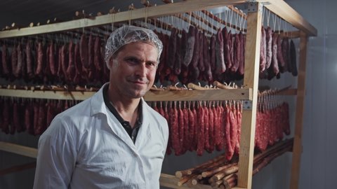 Handsome man butcher meat specialist worker standing at smokehouse on large organic meat farm. Sausages production. Professional workers. Portraits.