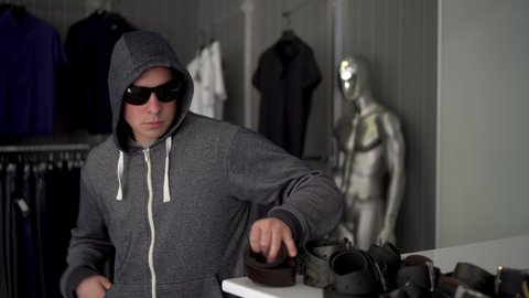 A man in a hood and glasses steals a belt from a store. Clothing store.