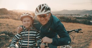 Father and son ride a bike. Happy cute boy in helmet learn to riding a bike in park on green meadow in summer day at sunset time. Family weekend. 4K video, Slow motion
