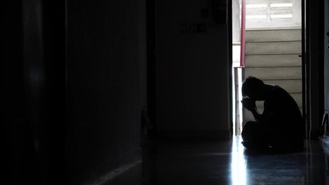 Silhouette of a sad man sitting in the dark leaning against the wall in old condo, Domestic violence, family problems, Stress, violence, The concept of depression and suicide