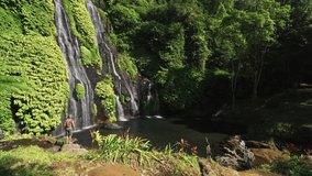 Active lifestyle traveler man standing on background Banyumala Waterfall is one of the most beautiful waterfalls in Bali located north of Lake Buyan. Indonesia. 4K Aerial video