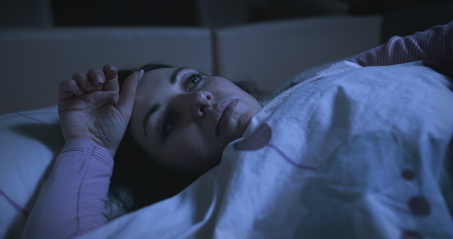 Sad pensive woman with an apathetic look lying on the bed and looking at the ceiling. Sleep problems, insomnia, thinking about her problems, can not sleep. Restless thoughts at night.  Royalty-Free Stock Footage #1059921344