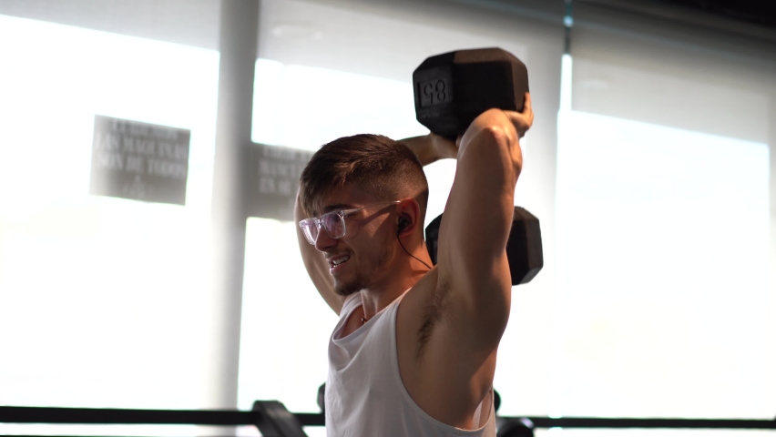 Young hip muscular man pumping iron behind head looking like he is straining.