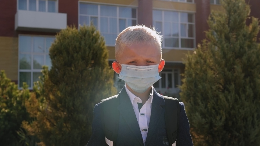 Portrait of a boy in a medical mask with a school backpack on the street, going to school after quarantine.