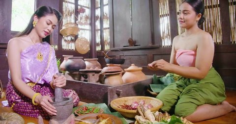 A beautiful asian female chef  dress on Ayutthaya cultural fashion sitting and cooking traditional thailand food in the vintage kitchen old style ancient house