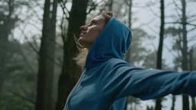 Arc Shot of Young Woman Standing in Forest and Turning around with Her Arms Spread Wide and Eyes Closed. She Enjoys Gentle Breeze, Breathes Deeply and Smiles Subtly. Slow Motion Cinematic Shot