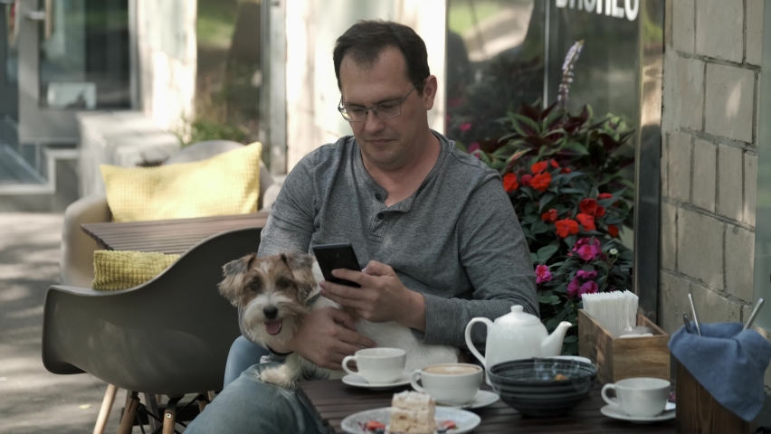 Man using mobile phone with small jack russell dog lying in his lap