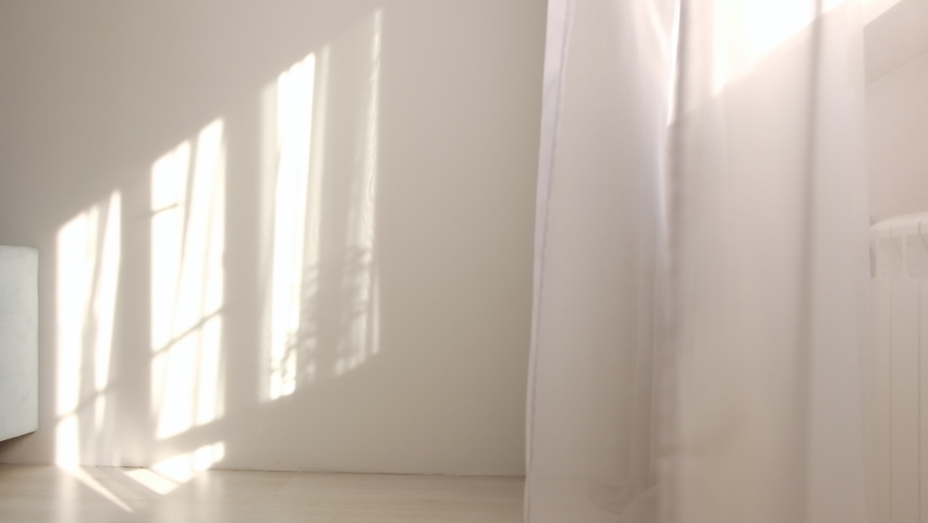 wind blows through the open window in the room. Waving white tulle near the window. Morning sun lighting the room, shadow background overlays. Royalty-Free Stock Footage #1059933737