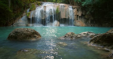 Erawan waterfall in Thailand. Peaceful natural background with beautiful waterfall in jungle rainforest with wet stones in water and natural pond pool
