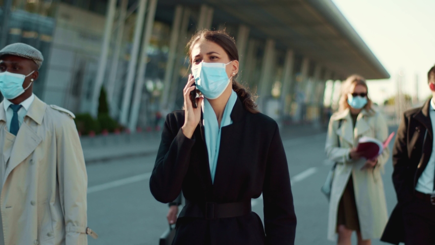 Young businesswoman walking with crowd of office people talking smartphone wearing protective face masks going to work outdoors. Social distancing. Quarantine. - Powered by Shutterstock - Get 15% off with code: PIKWIZARD15