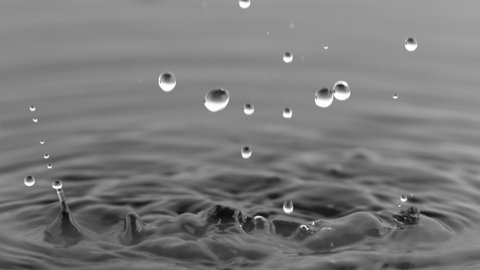 Super Slow Motion Shot of Water Drops Falling into Water on Black Background at 1000 fps.