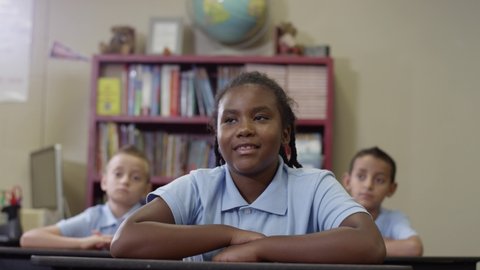 Primary students in uniforms sit in class as happy black girl raises her hand