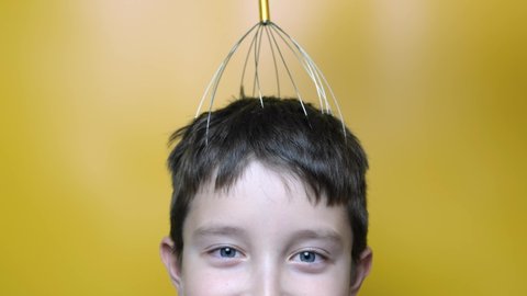 A caucasian boy enjoy head scalp massage by anti stress acupuncture metal octopus tool, equipment, she closes her eyes with pleasure, yellow background, close up view.