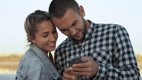 Beach. Evening. A couple of young people in love look into a smartphone and smile. - Powered by Shutterstock - Get 15% off with code: PIKWIZARD15