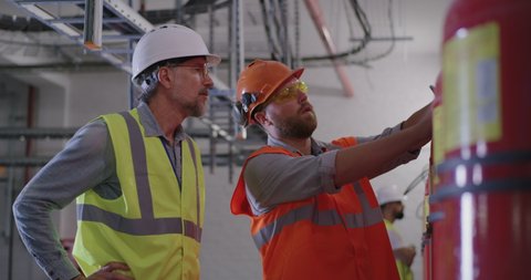 Bearded worker demonstrating fire extinguishers to mature inspector while working on power station