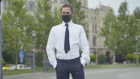 Portrait of sad man in Covid-19 face mask showing empty pockets. Unemployed Caucasian young businessman having no money during coronavirus pandemic lockdown. Poverty concept.