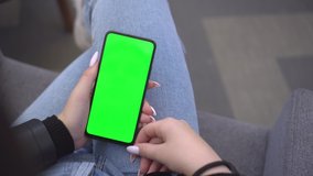 Shopping center. Back view of brunette holding chroma key green screen smartphone watching content. Gadgets and contemporary people concept.
