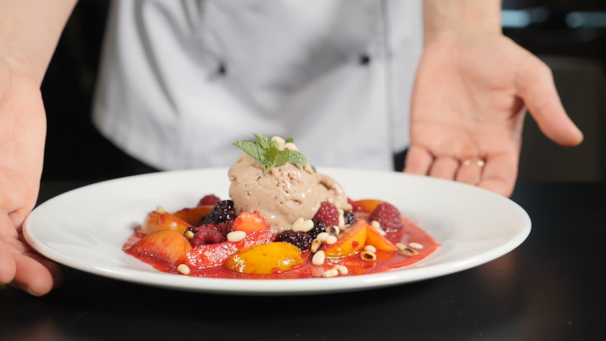 Restaurant food concept. chef presenting food plate with delicious flambe style fruit dessert. Close-up. Restaurant food cooking and serving. Chef hands holding white plate and putting on black table | Shutterstock HD Video #1059950726