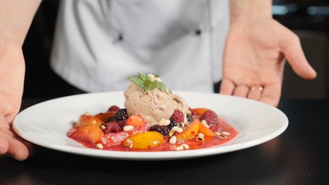 Restaurant food concept. chef presenting food plate with delicious flambe style fruit dessert. Close-up. Restaurant food cooking and serving. Chef hands holding white plate and putting on black table