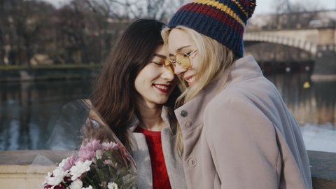 Close-up portrait of happy lesbians on date. Blonde girl giving asian girlfriend bunch of flowers. Young homosexual couple spending time together on holiday of valentine day. Romantic, LGBTQ concept. ஸ்டாக் வீடியோ