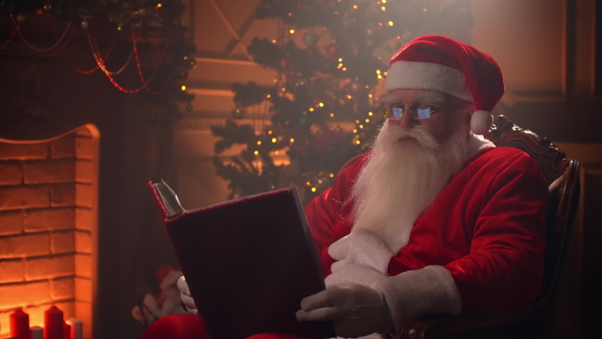 Santa Claus sitting at his room at home near Christmas tree and resting by his fireplace. | Shutterstock HD Video #1059957254