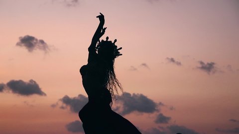 Side view of sexy, elegant and erotic arabian woman performing belly dance on the beach during golden hour. Silhouette. Slow motion.
