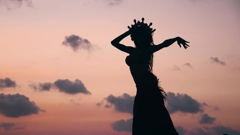 Close up of sexy, elegant and erotic arabian woman performing belly dance on the beach during golden hour. Silhouette. Side view.