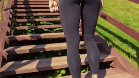 Fit caucasian woman stands in front of wooden staircase in city park ready for outdoor exercise. Rear view. Sport background. Slow motion video. Overcoming obstacles theme.