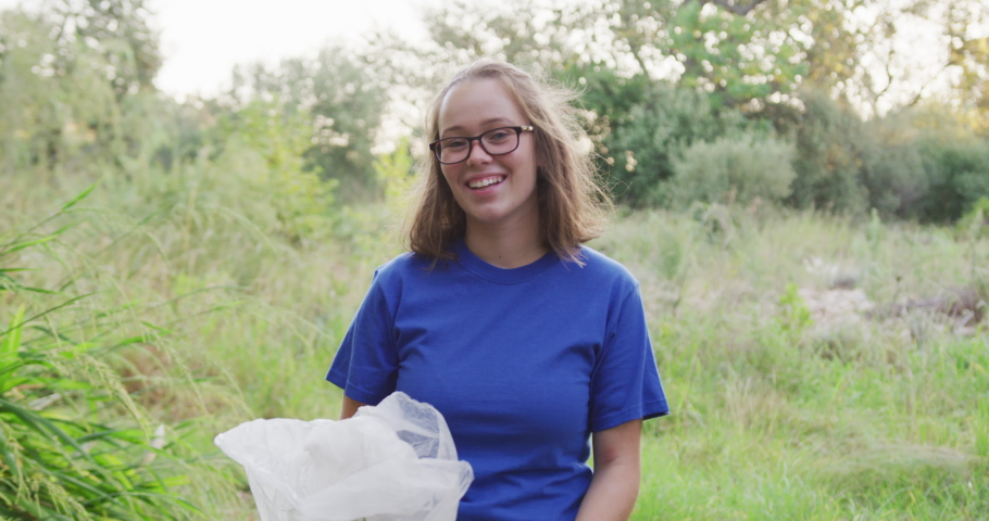 Portrait of a happy female Caucasian volunteer cleaning up a river in the countryside, holding a rubbish bag, smiling and looking at camera. Ecology and social responsibility in a rural environment.