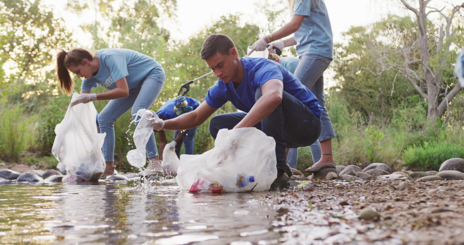 A multi-ethnic group of conservation volunteers cleaning up a river on a sunny day in the countryside, picking up rubbish. Ecology and social responsibility in a rural environment. Royalty-Free Stock Footage #1059969776