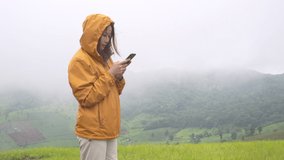 Woman tourist in yellow jacket standing on mountain peak using smartphone with internet for outdoor online working or social media. Female enjoy hiking with wireless technology on travel vacation.