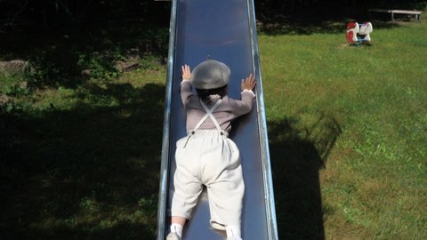 A funny little girl playing on a slide in the park. Slide down in prone position with head up. Top view