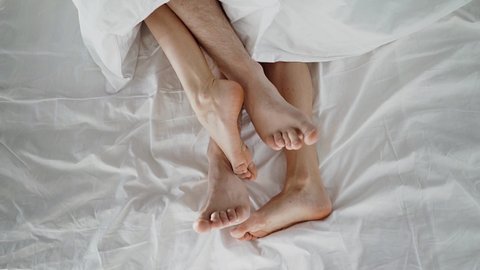 Couple in bed making love. male and female legs top view, white linens. 