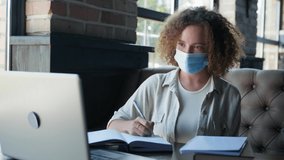 health care, young charming woman in medical mask takes precautions and wears medical mask on face during online distance training sitting in cafe by window