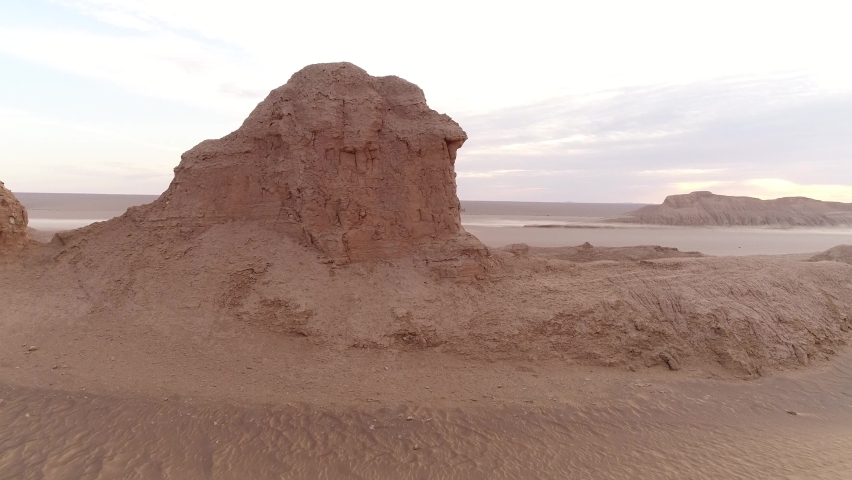 Dolly shot from the formation of sandstones in dasht e lut desert at the morning with cloudy sky and flat ground in background, aerial shot the formation of kalut in shahdad desert, iran | Shutterstock HD Video #1059975989