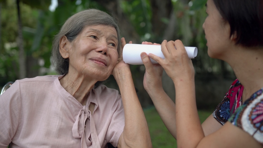 Daughter talking to hearing impaired elderly woman , using paper tube