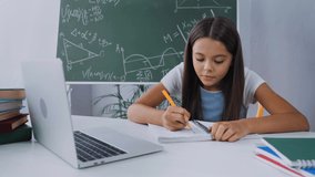 schoolkid writing in notepad while e-learning at home