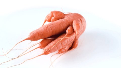 Ugly carrot rotate on a white background. Funny, unnormal vegetable or food waste concept. Horizontal orientation